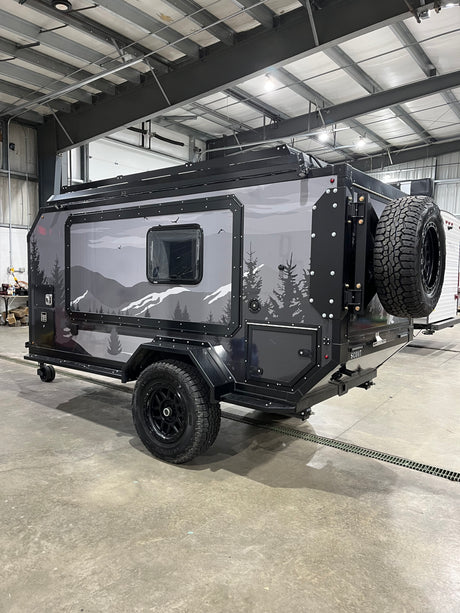 A rugged off-road camper trailer, ideal for rv rental adventures. Features unique mountain graphics and a rear-mounted spare tire.