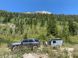  perfect for an RV rental adventure.|Adventure awaits! Silver SUV & Mission Overland RV rental traverse a rocky creek for off-road camping.|Off-road desert camping setup featuring an expedition trailer