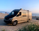 Enjoy beach travel! RV rental: a light gray Mercedes Sprinter camper van on a sandy path next to the ocean at sunset.