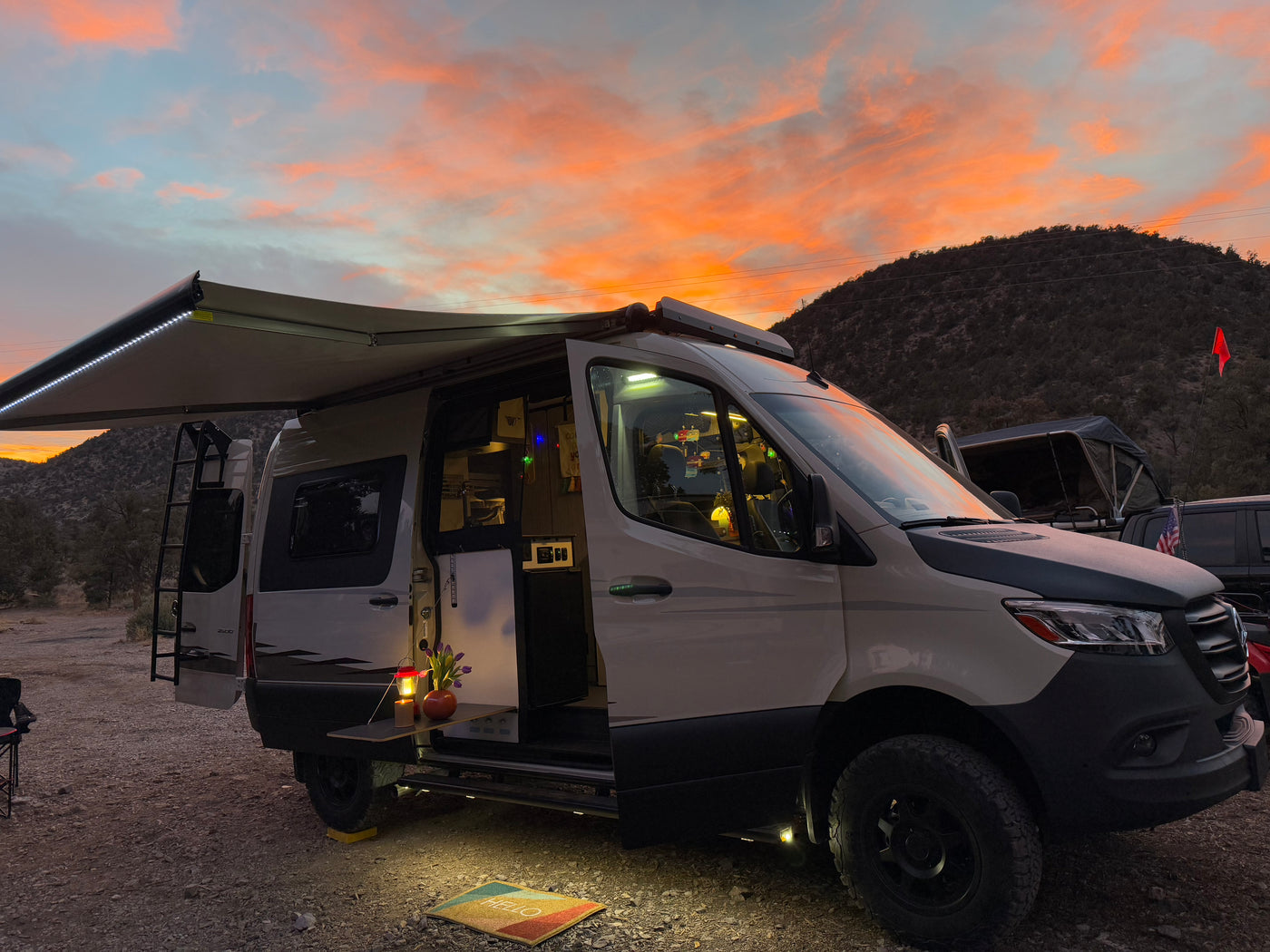 Gorgeous sunset over an RV rental camper van campsite. Awning extended, lights on, revealing a welcoming outdoor setup.