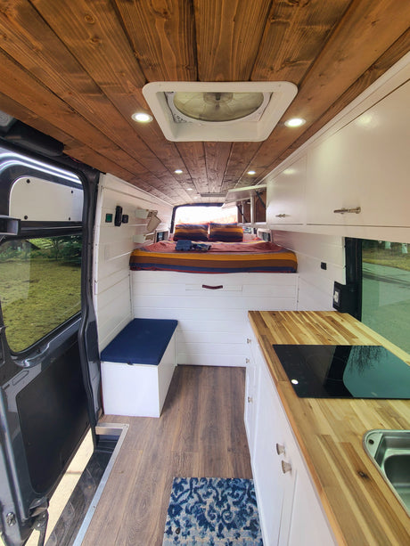 Cozy RV rental interior showcasing a full bed, compact kitchen with cooktop, and bright living space with wood ceilings.