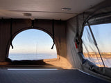 RV rental interior with stunning ocean views from pop-top clear and mesh windows. Includes a bed for coastal camping.