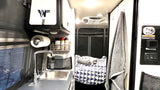 Cozy RV rental interior shows a compact kitchen with sink, paper towel holder, spices, and a geometric-patterned bed.