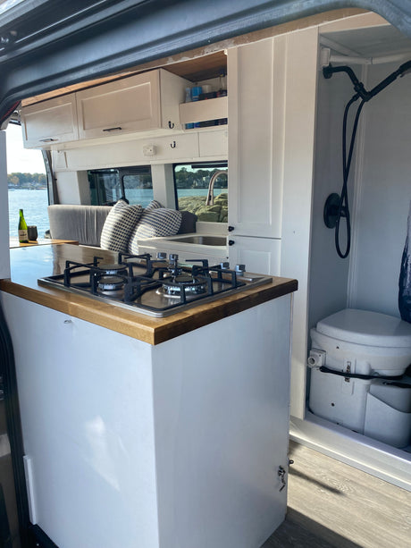 RV rental: Van interior features a kitchen with stovetop, sink, overhead cabinets, shower, toilet, and scenic water view.