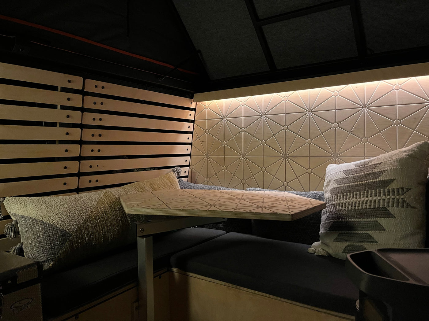 Cozy RV rental interior with patterned wood walls, slatted accents, and a matching table over dark bench seating. — photo 8
