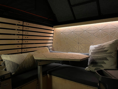 Cozy RV rental interior with patterned wood walls, slatted accents, and a matching table over dark bench seating.