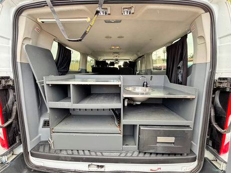 RV rental camper van's custom kitchen features a sink, faucet, shelves, drawers, & folding table for travel convenience.