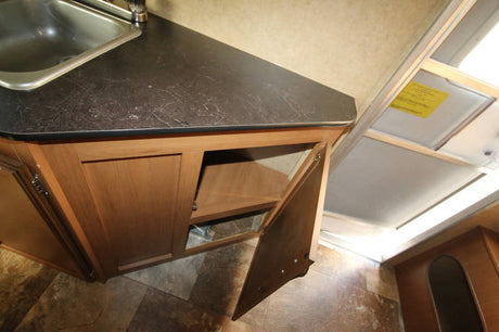RV rental interior: corner kitchen with sink, dark countertop, and open wood cabinet for storage.