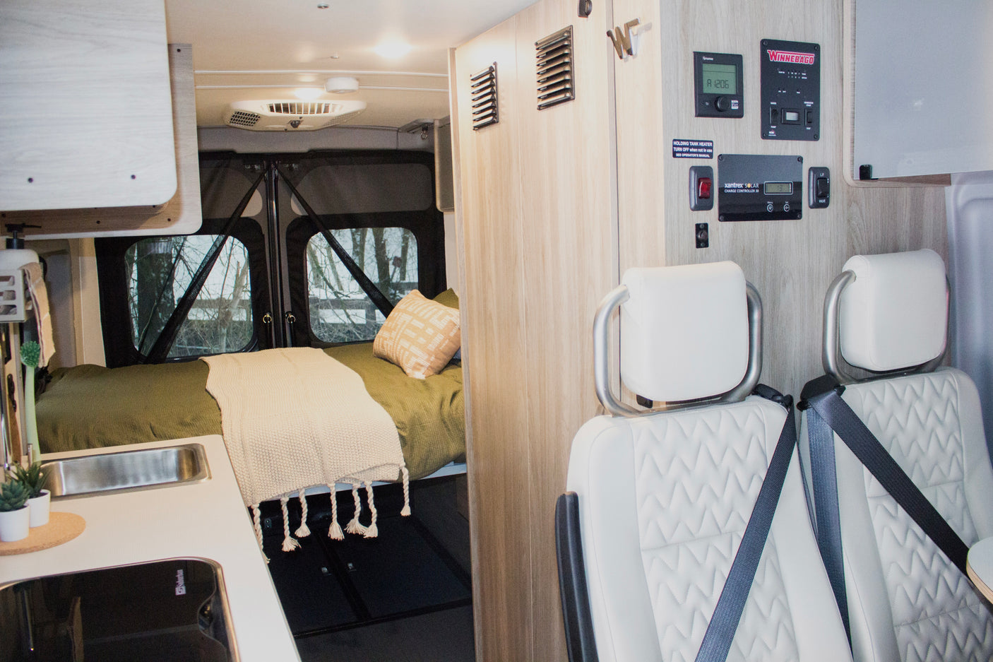 Explore the cozy interior of this RV rental, featuring a bed, kitchenette, passenger seats, and essential controls.