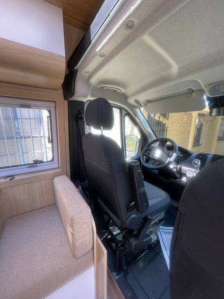 Experience a comfortable RV rental. View of the driver's cabin and interior living space with light wood accents and window.