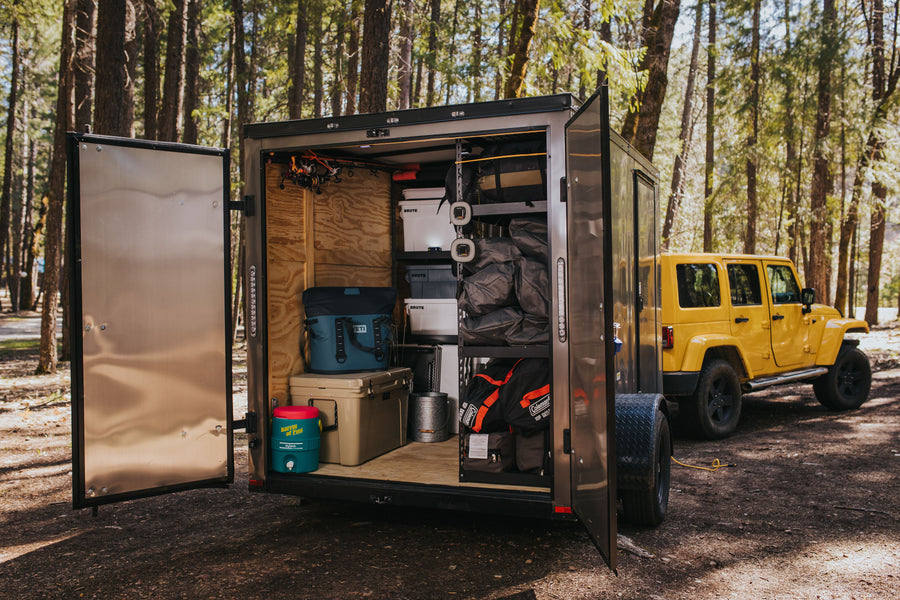 A custom camping trailer, packed with gear like Yeti coolers & Coleman sleeping bags, towed by a Jeep. Ideal for an RV rental alternative.