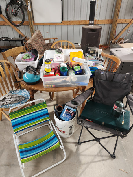 RV rental prep: Table of camping gear, including a portable stove, chairs, kitchen supplies, and a kettle.