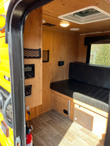 Cozy RV rental interior with wood paneling, bench seating, control panel, and roof vent, perfect for compact living.