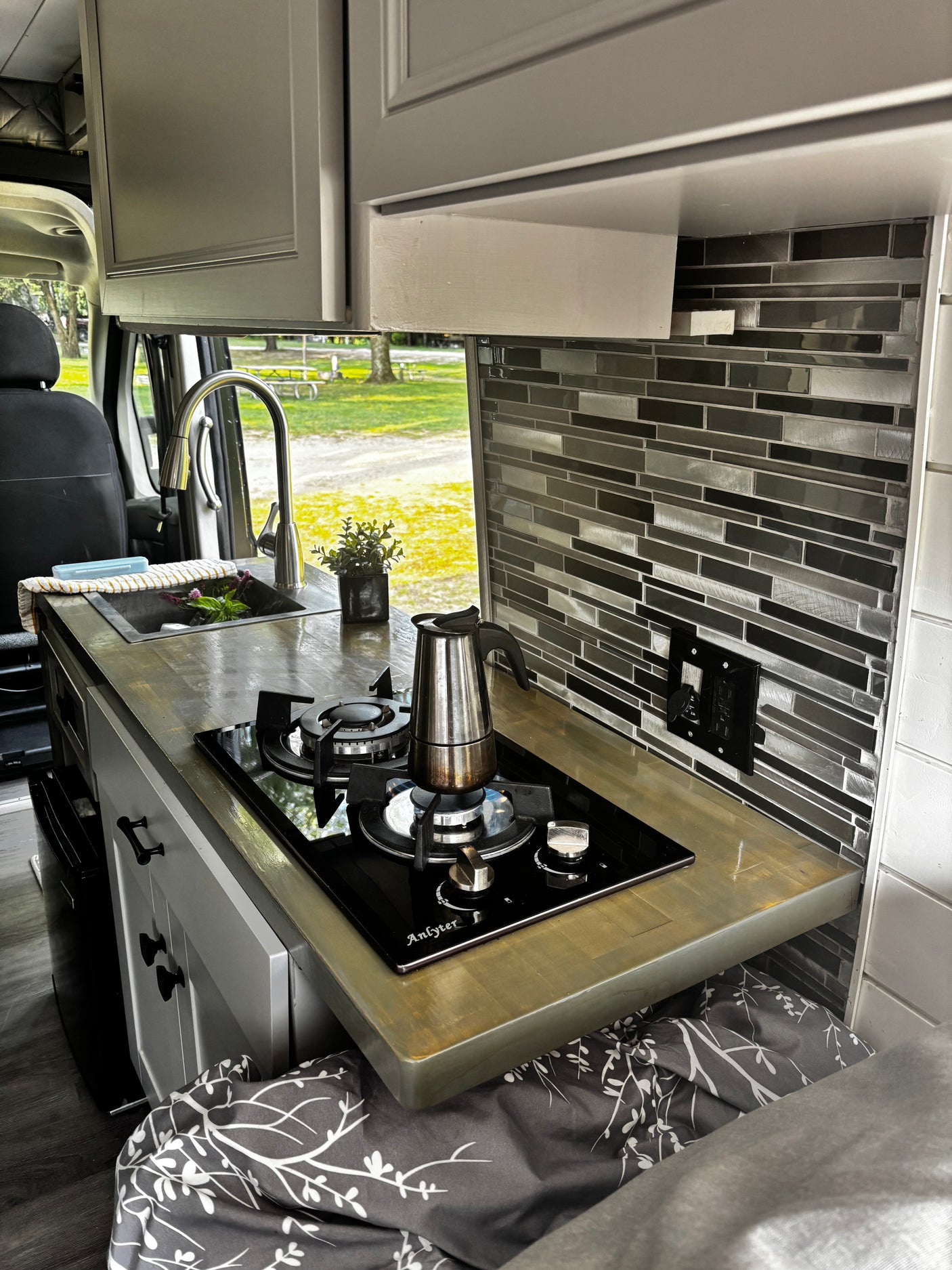 Compact RV rental kitchen with sink, Anlyter stove, Moka pot, and tiled backsplash. Ideal for van life adventures.