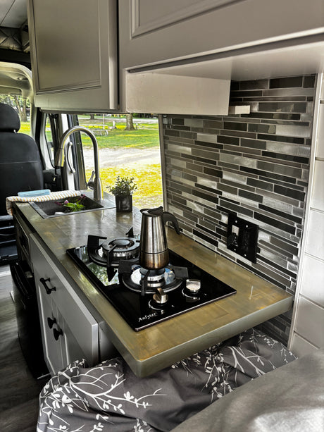 Compact RV rental kitchen with sink, Anlyter stove, Moka pot, and tiled backsplash. Ideal for van life adventures.