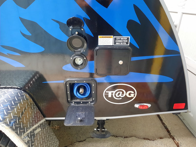 This RV rental shows the side of a T@G camper with various utility hookups, including water, power, and an outdoor shower hose. — photo 7