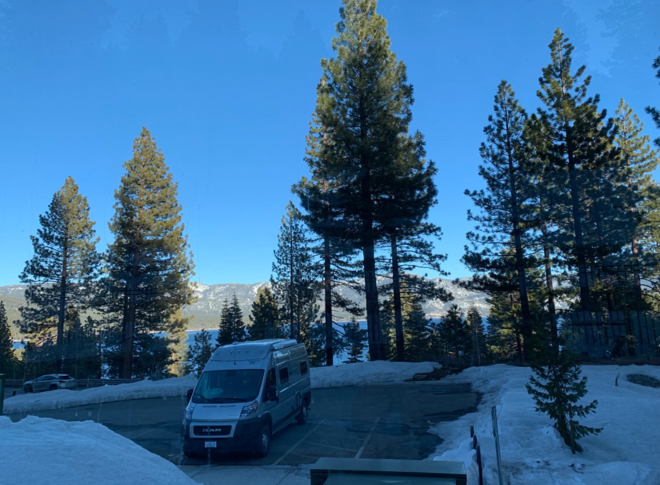 RV rental parked in a scenic winter landscape with a lake, snow-capped mountains, and tall pine trees under a blue sky. — photo 20