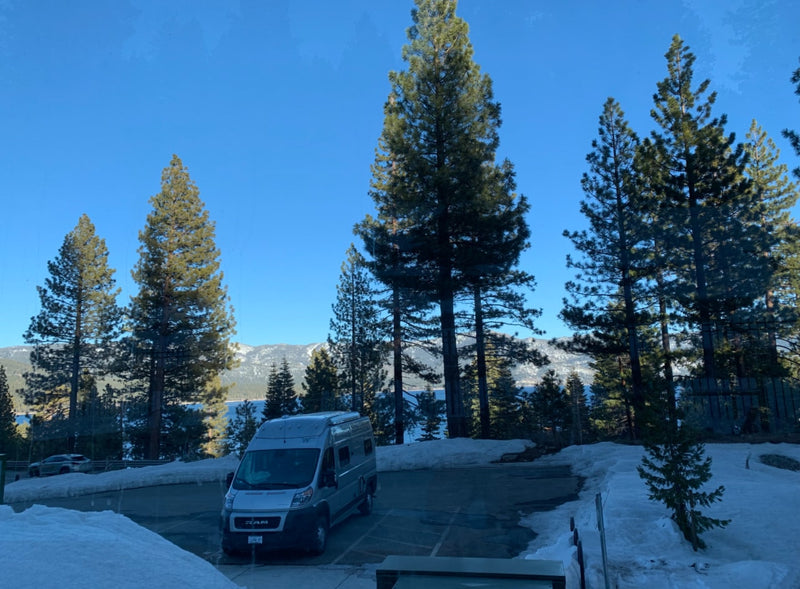 RV rental parked in a scenic winter landscape with a lake, snow-capped mountains, and tall pine trees under a blue sky. — photo 20