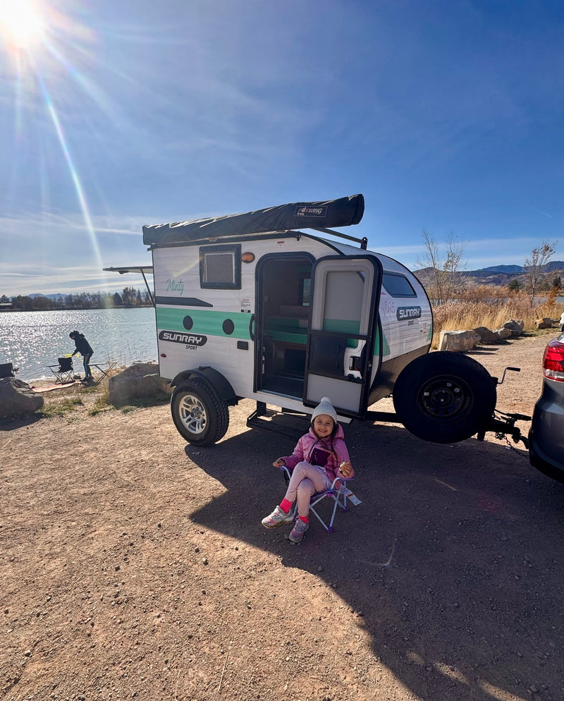 A young girl enjoys the outdoors by an rv rental, a Sunray Sport camper, parked by a sunny lake. A person fishes nearby. — photo 11