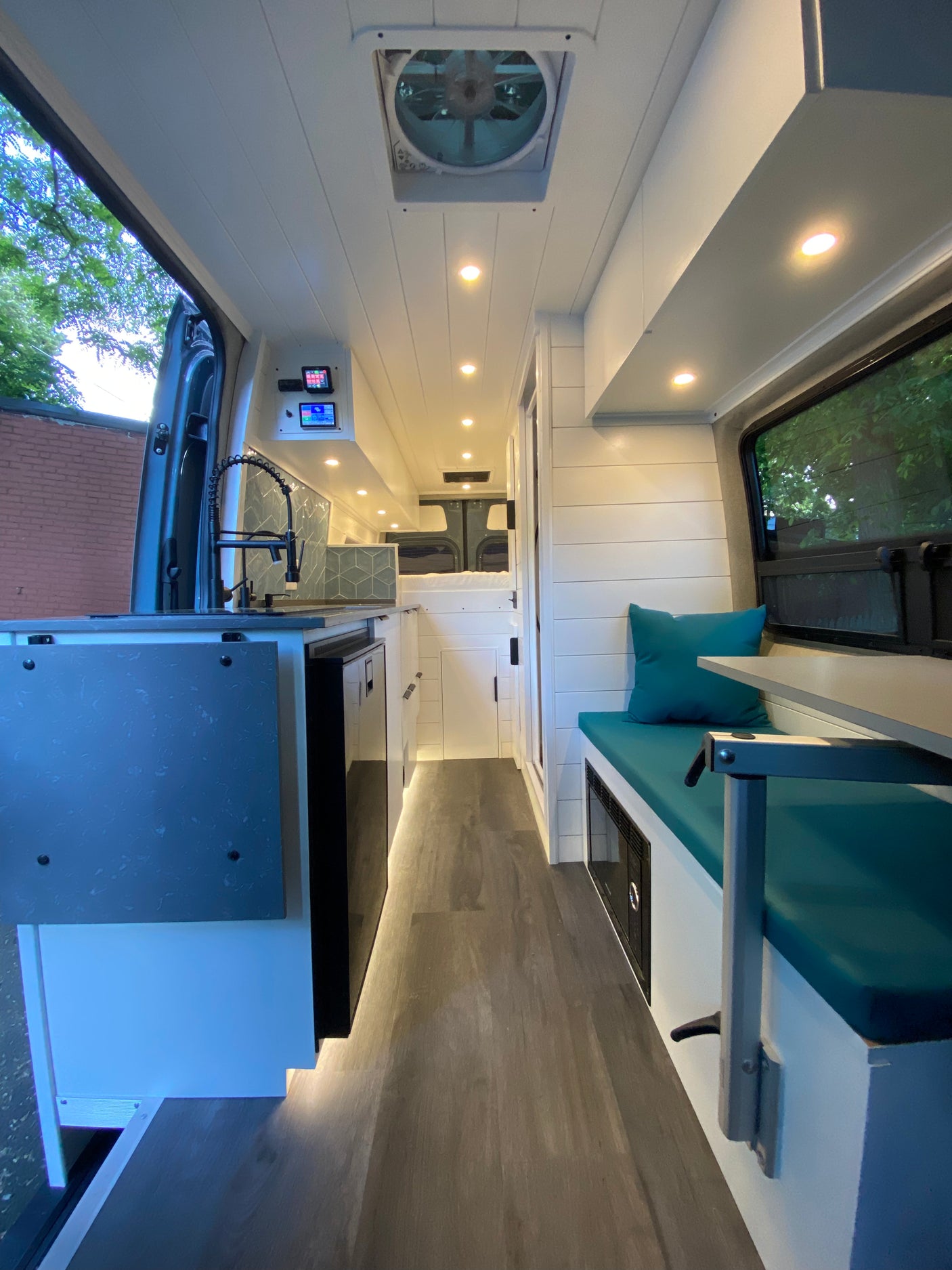 Modern custom rv rental interior: bright kitchenette with tiled backsplash, seating area, and rear bed in a sleek camper van.