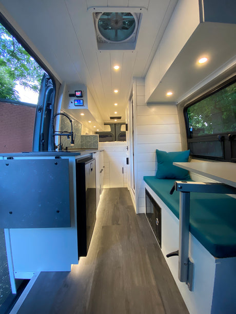 Modern custom rv rental interior: bright kitchenette with tiled backsplash, seating area, and rear bed in a sleek camper van.