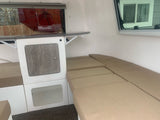 Compact RV rental interior featuring a kitchenette with fold-out table, comfy bench seating, and ample light from side windows.