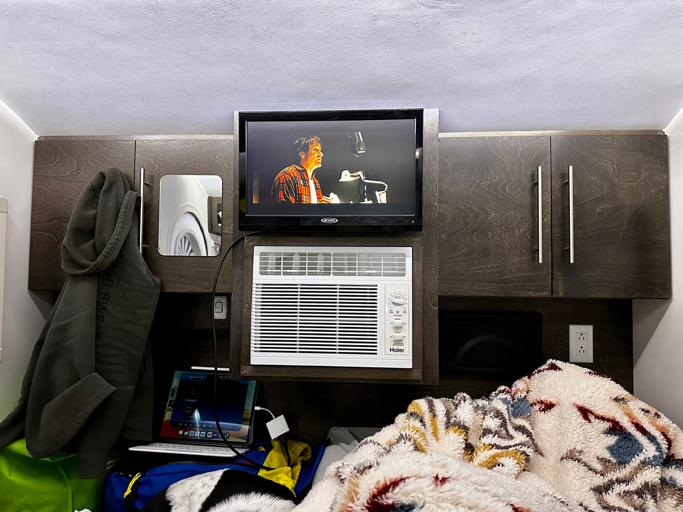 Cozy rv rental interior featuring a textured ceiling, Jensen TV, Haier AC, wood cabinets, and a plush blanket.
