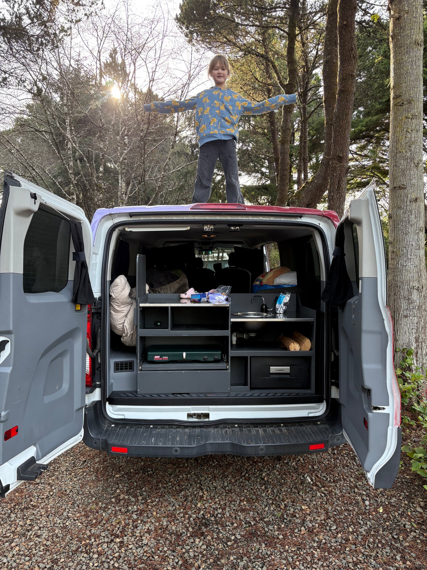 Child enjoys freedom on top of a fully-equipped RV rental camper van, revealing its outdoor kitchen for camping adventures.