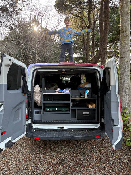 Child enjoys freedom on top of a fully-equipped RV rental camper van, revealing its outdoor kitchen for camping adventures.