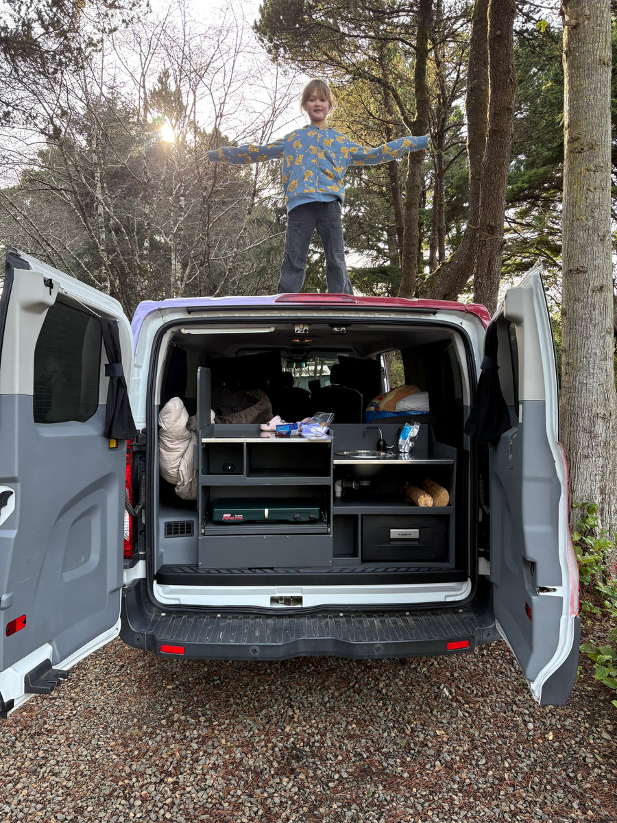 Child enjoys freedom on top of a fully-equipped RV rental camper van, revealing its outdoor kitchen for camping adventures.