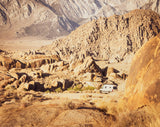 An RV rental van is perfectly parked amidst large desert rock formations, with towering mountains in the distance.