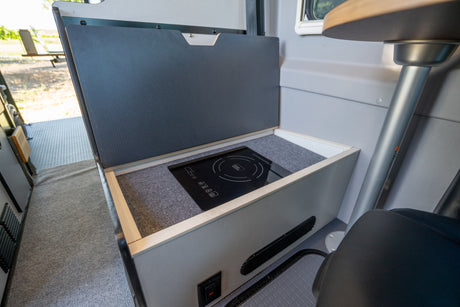 Inside an RV rental: a compact camper van kitchen featuring a sleek, built-in induction cooktop with its cover open.