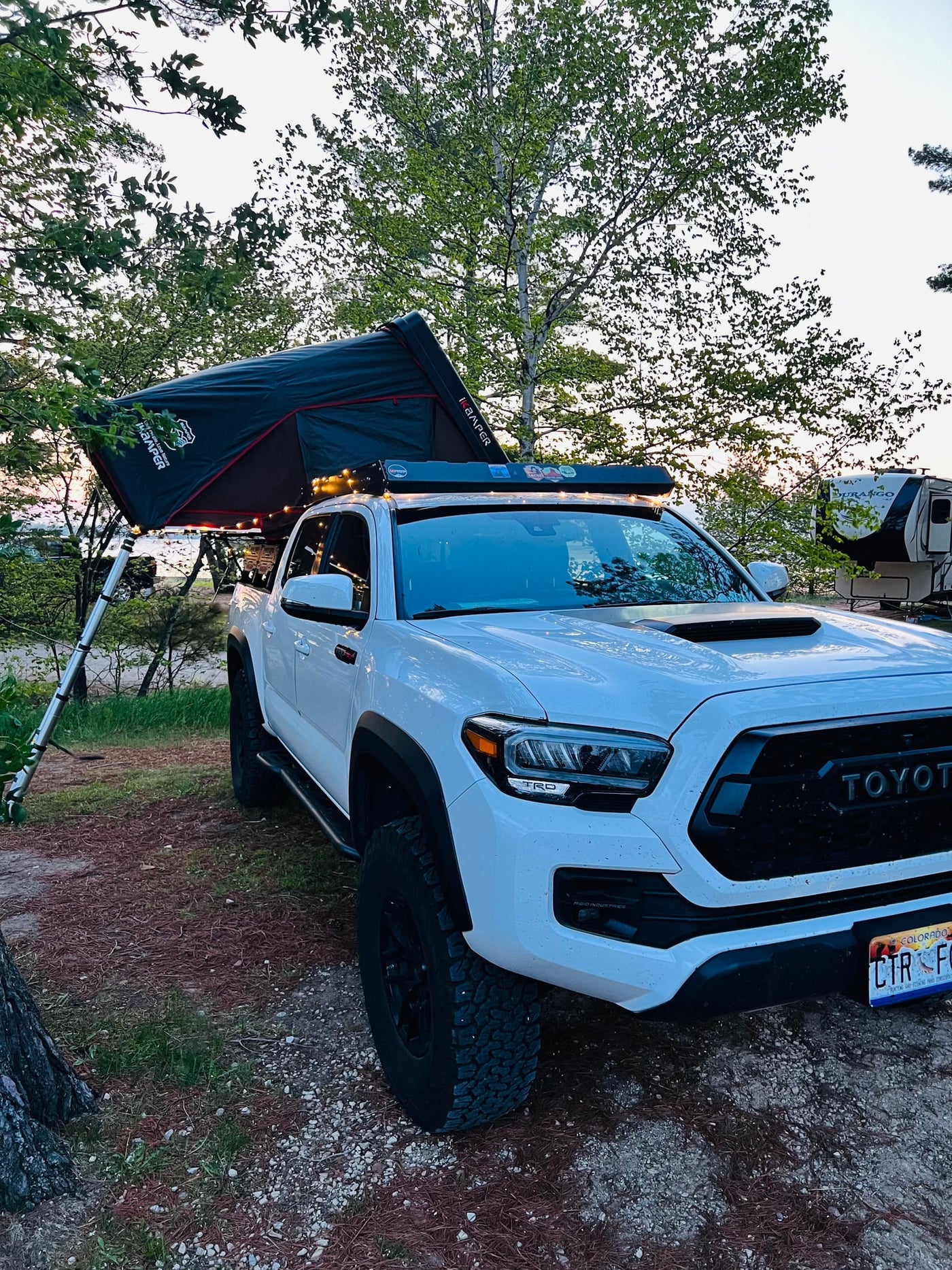 White Toyota Tacoma truck with an iKamper roof-top tent, set up for camping next to an RV rental by the water, for an overlanding adventure. — photo 3