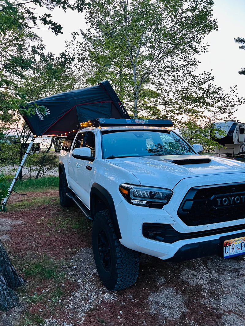 White Toyota Tacoma truck with an iKamper roof-top tent, set up for camping next to an RV rental by the water, for an overlanding adventure. — photo 3