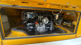 RV rental: Rear engine bay of a yellow VW, showing the air-cooled flat-four engine, carburetor, distributor, and a Duralast battery.