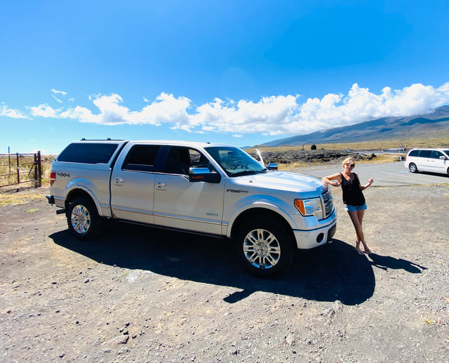 Silver Ford F-150 with camper shell & happy traveler on a volcanic road. Great for an rv rental adventure!