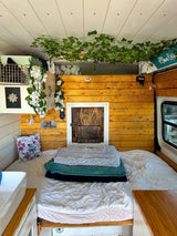 Cozy RV rental bedroom with custom wood paneling, a comfy bed, and green ivy decor for a relaxing stay.