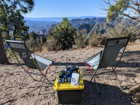 Scenic RV rental campsite features two chairs, coffee setup, and vast canyon views. Ideal outdoor relaxation.