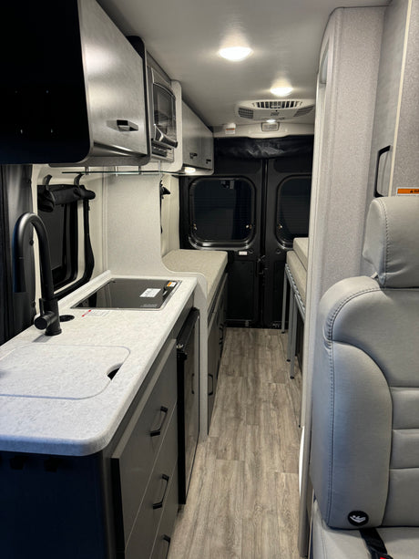 Modern camper van RV rental interior featuring a sleek kitchen with sink, stove, microwave, and rear living space.