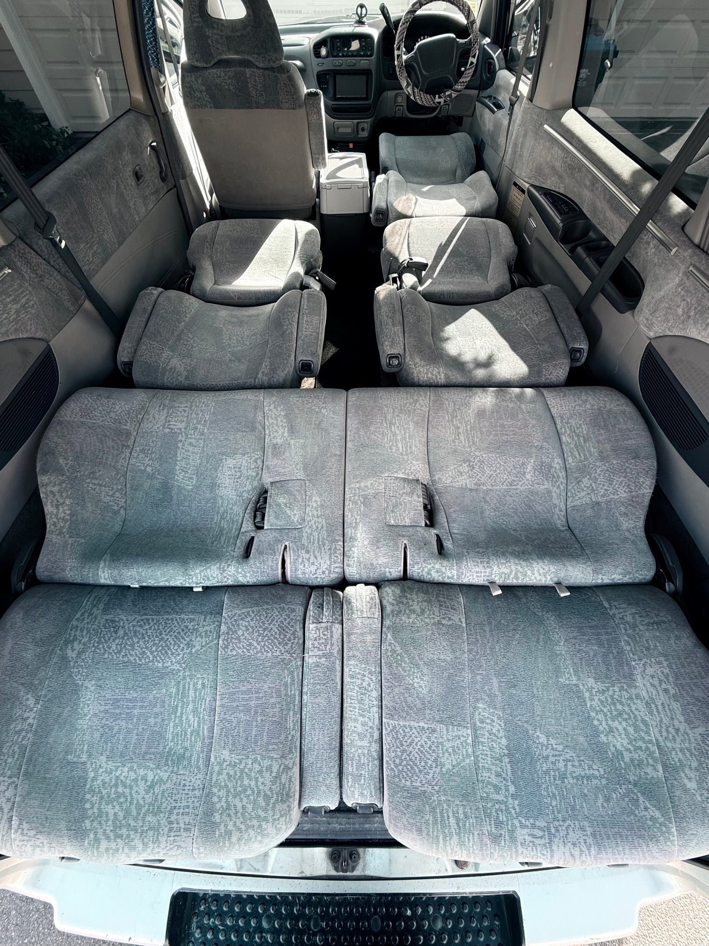 Spacious rv rental interior: multiple rows of grey fabric seats are folded flat, forming a large, comfortable sleeping area.