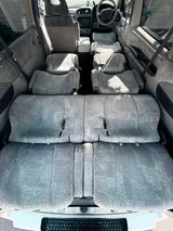 Spacious rv rental interior: multiple rows of grey fabric seats are folded flat, forming a large, comfortable sleeping area.