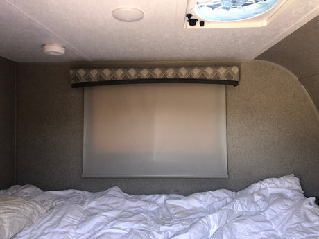 Cozy RV rental bedroom interior with rumpled bed, window shade, and ceiling vent. Ready for adventure.