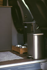 RV rental amenities: a stainless steel trash can, pet food/water bowls on a stand, and a floor mat. Functional interior.