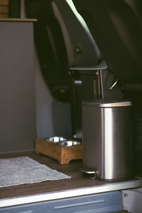 RV rental amenities: a stainless steel trash can, pet food/water bowls on a stand, and a floor mat. Functional interior.