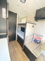 RV rental interior features bunk beds, a cozy dinette with a mountain pillow, and a compact kitchen area.
