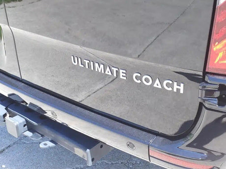 Rear of a dark Ultimate Coach RV, ideal for an RV rental. Features a tow hitch and bumper sensors.