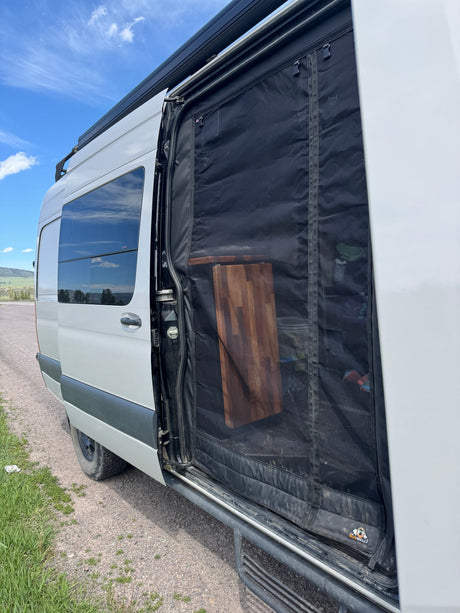 RV rental camper van with side door open, featuring a bug screen for fresh air. A wooden cutting board is visible inside.