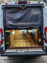 Open rear of an RV rental camper van, revealing its custom wood interior with storage, bed slide-out, and mesh screen.