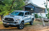 Grey Toyota Tacoma pickup with a rooftop tent set up for camping near the ocean. Perfect for your RV rental adventure.