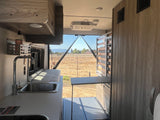 Cozy rv rental interior with kitchen, bed, and a wide-open view of a dry field and distant mountains.